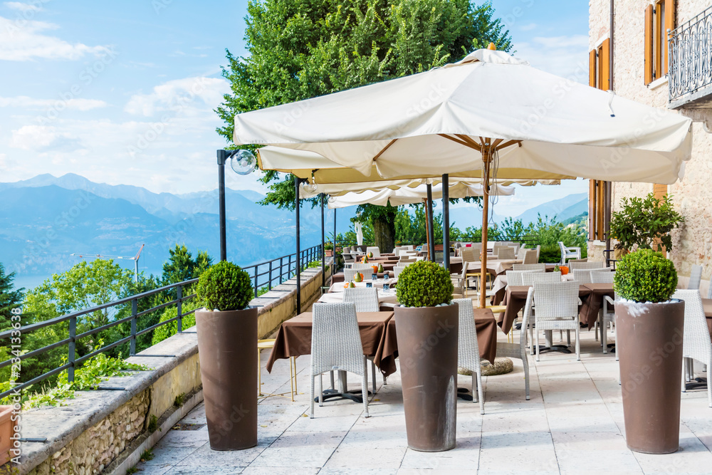 Cozy Italian Restaurant with White Umbrellas and Tables with Lake and Mountain View in Italy 