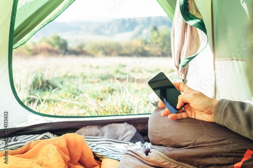 Traveler uses mobile phone sitting in tent. Close up image man hands with mobile phone