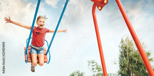 Happy little child girl laughing and swinging on a swing in the city park in summer