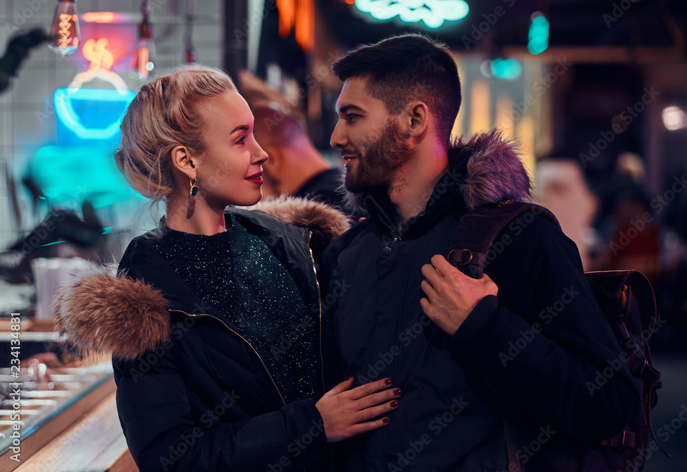 Attractive couple in love. A beautiful girl hugging her boyfriend standing in the night on the street.