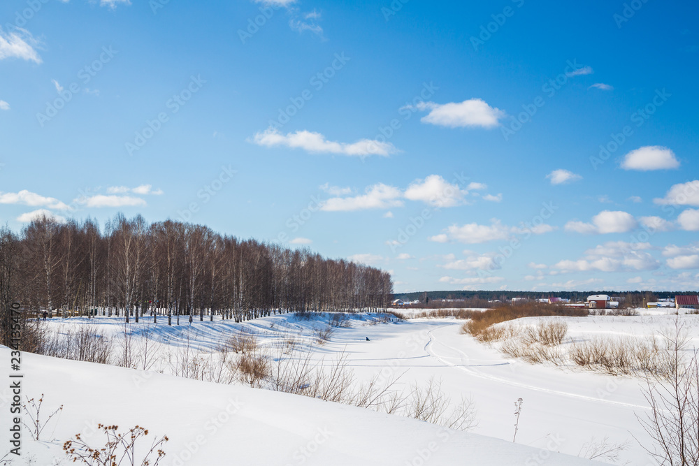 Winter landscape. Countryside. Frozen river. Sunny day. Blue sky. White clouds.