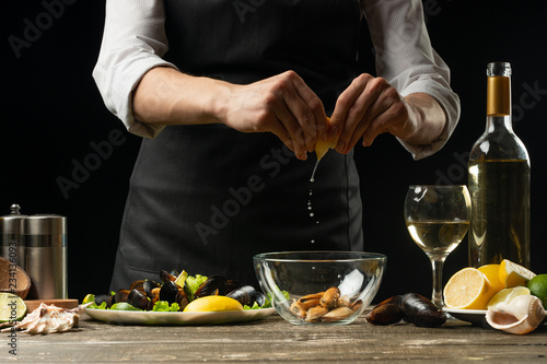 Chef pouring lemon juice with mussels with white wine salad on a dark background