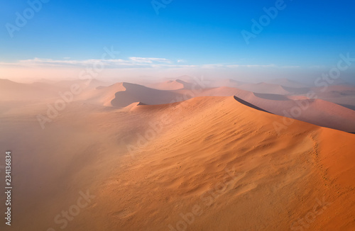 Panoramic, aerial, artistic photo of Namib dunes. Early morning Namib desert covered in mist. Orange dunes of Namib from above. Desert landscape. Sunrise in Namib-Naukluft desert. Traveling Namibia.