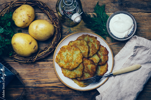 Pan-fried potato pancakes (rosti, kartoffelpuffer, latkes, draniki, hash browns): traditional potato fritters on a wooden background with sourcream and greens photo