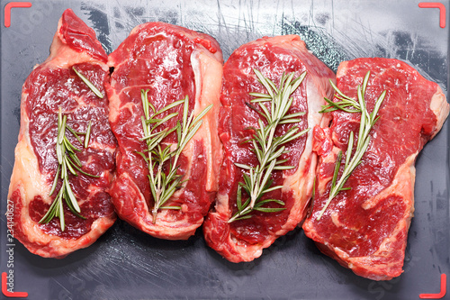 Raw beef steak with rosemary on a dark wooden table.