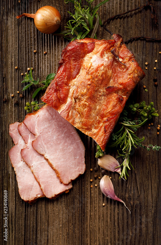 Smoked meats, sliced smoked pork loin on a wooden  table with addition of fresh  herbs and aromatic spices, top view.  