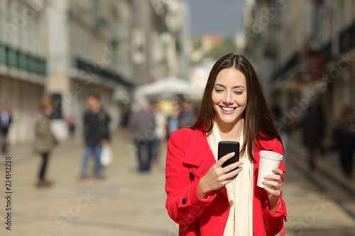 Front view of a happy woman using phone in winter