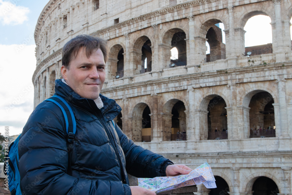 Handsome traveler looking at tourist map in Rome in front of Colosseum. Backpacker with camera and tourist map.