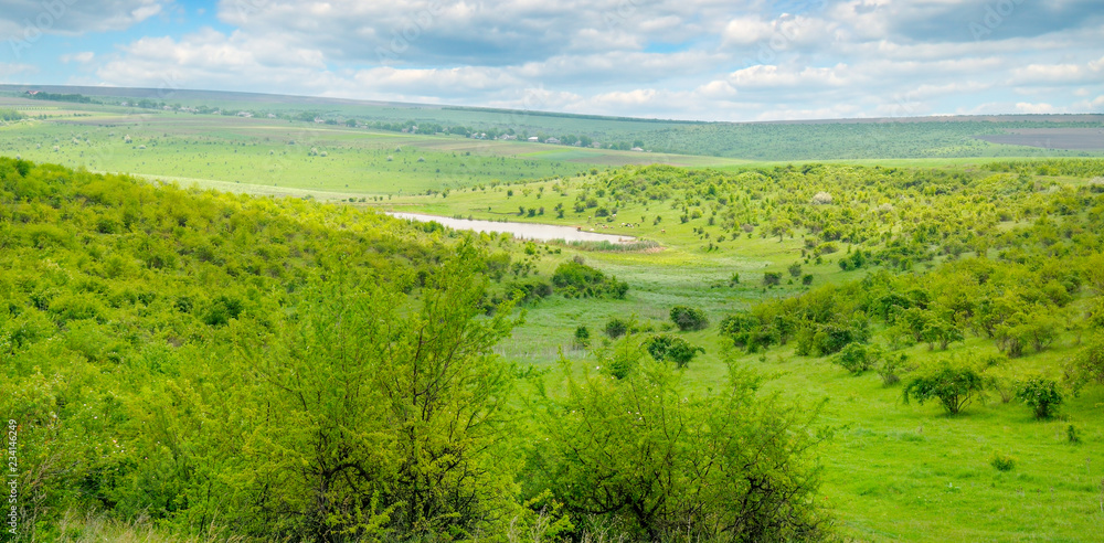 Green field and blue sky. Picturesque hills formed by an old river terrace. Moldova. Agricultural landscape. Wide photo.