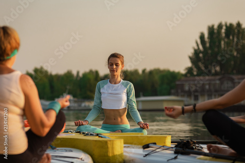 Group of women sitting on paddleboard and practicing yoga meditation