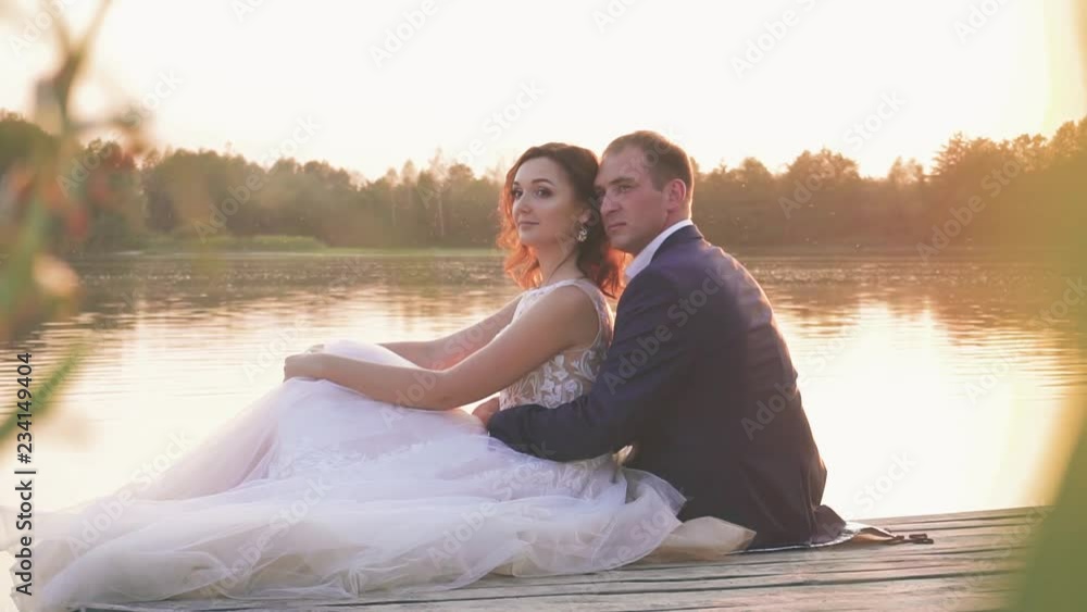 young couple in love near the river at sunset on the pier, the bride in a wedding dress with the groom young couple in love near the river at sunset on the pier, the bride in a wedding dress with the groom
