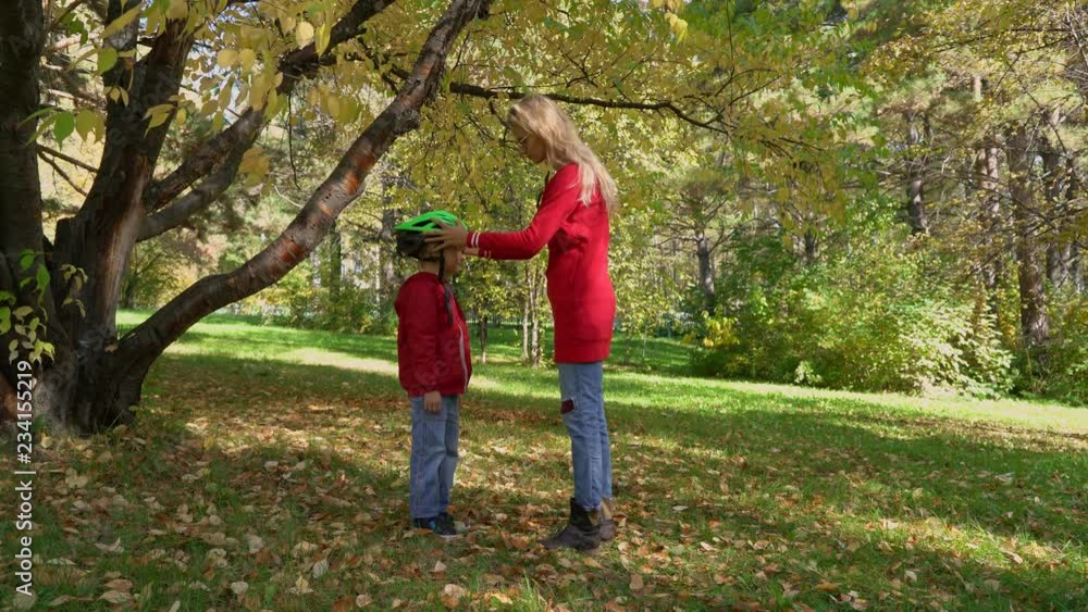 Mother wearing bicycle helmet on little boy in autumn park Mother wearing bicycle helmet on little boy in autumn park