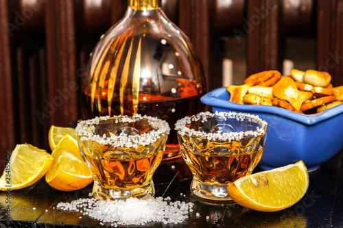 Tequila shots with salt, lemon and snacks. Mexican gold tequila in short glasses on wooden table.