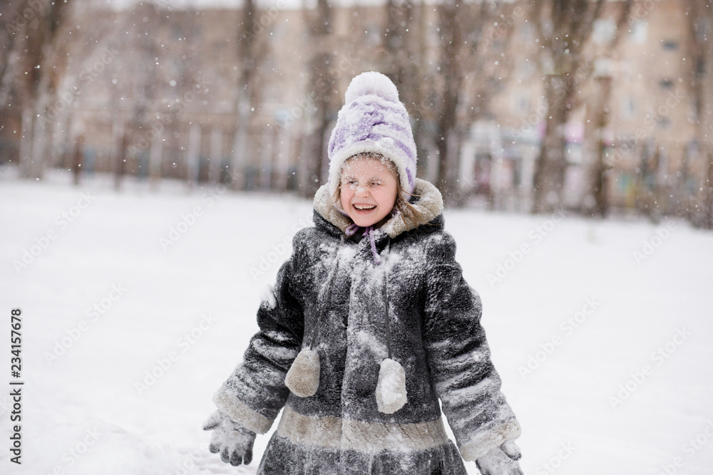 Cute little girl covered with snow has fun in winter park,