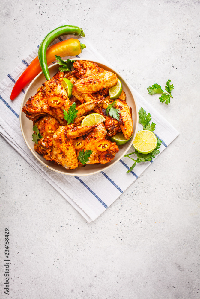 Spicy grilled chicken wings in tomato sauce in a white plate on a white background.