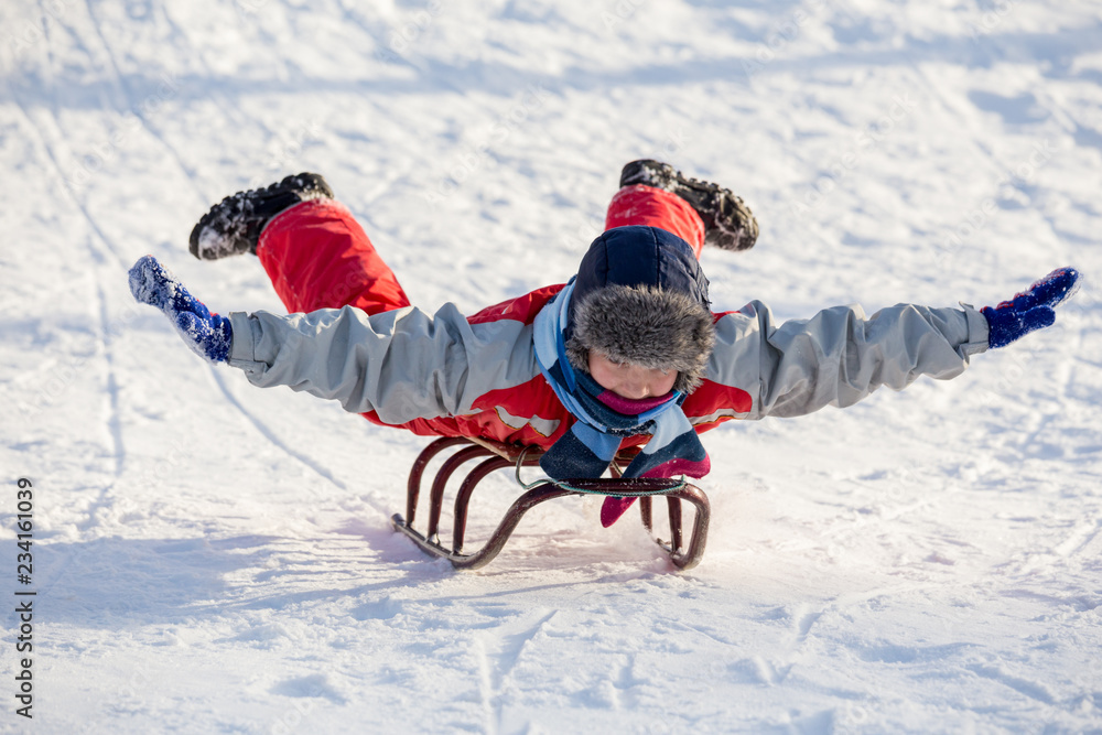 happy boy riding at the sledge on snowy hill