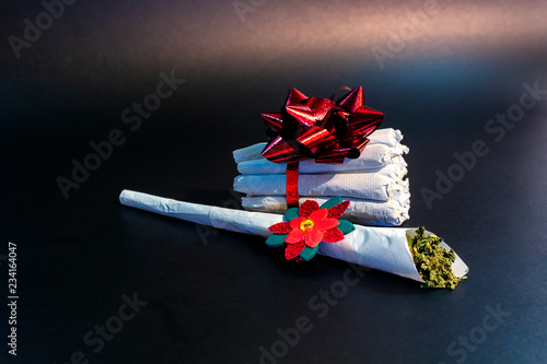 Obraz na płótnie A large marijuana joint with a festive decoration on it in front of a bundle of joints tied in ribbon and a bow isolated. w salonie