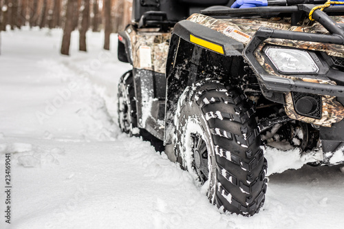 Close-up ATV 4wd quad bike in forest at winter. 4wd all-terreain vehicle stand in heavy snow with deep wheel track. Seasonal extreme sport adventure and trip. Copyspace