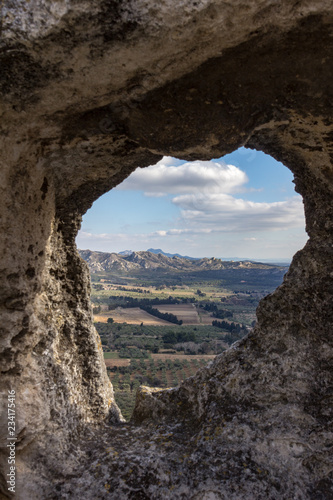 The valley between Les Baux de Provence and the Alpilles mountains are dotted with farms as viewed through a natural frame in the wall