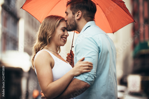 Romantic couple standing under an umbrella in street