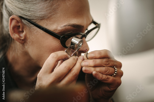 Mature female jeweler looking at stone through loupe photo