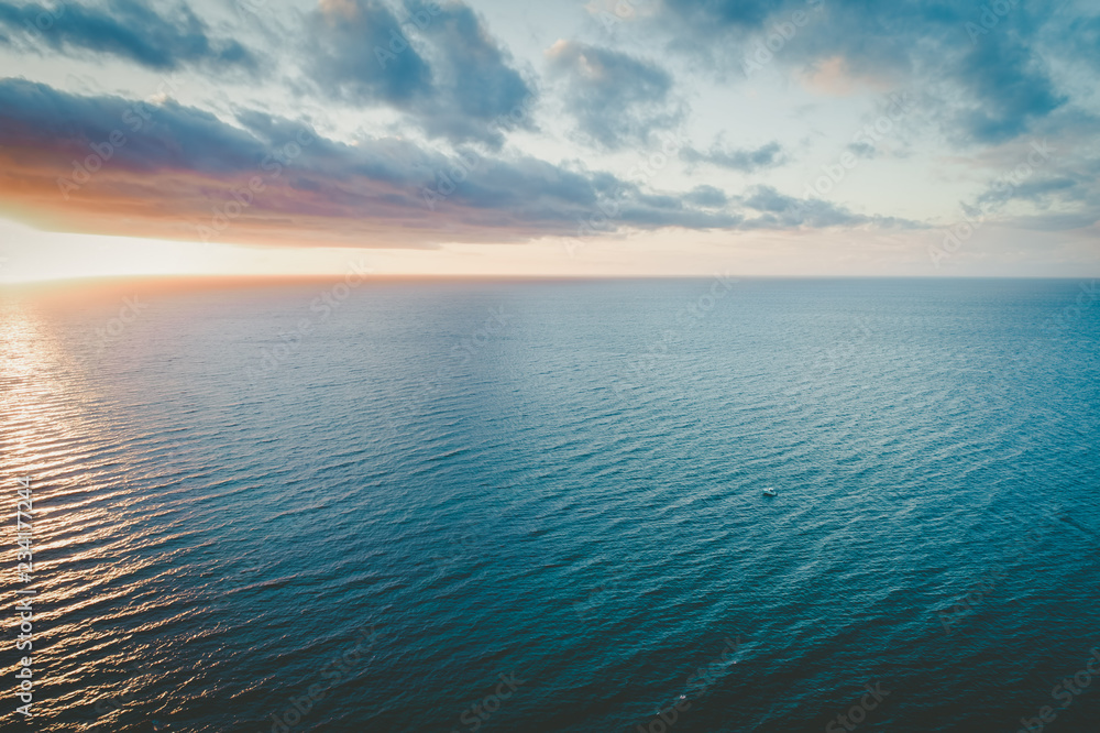 Lonely boat sailing calm ocean waters at sunset - aerial view