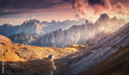 Landscape with majestic mountains, house, dramatic sky with red clouds and yellow sunlight at sunset. Autumn scenery with mountain valley in Tre Cime park in Dolomites, Italy. Italian alps in fall