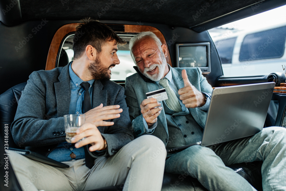 Senior and young businessman in limousine and working together.