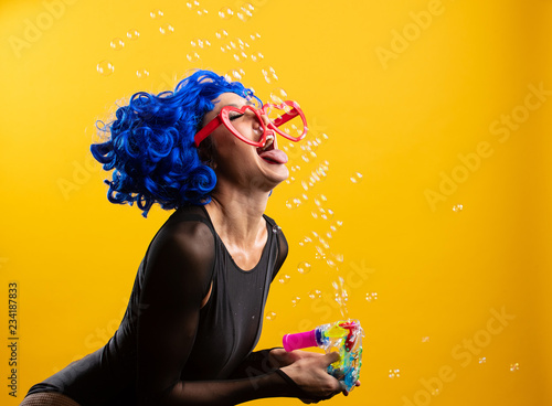 Woman with colorful blue hair blowing and popping bubbles