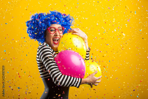 Colorful fun portrait of woman with balloons and confetti in front of yellow background