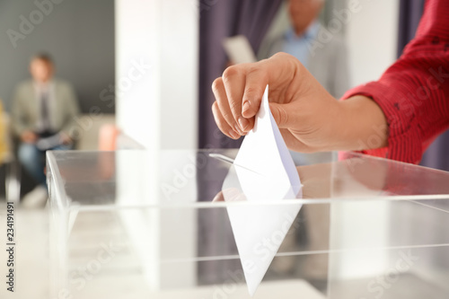 Woman putting ballot paper into box at polling station, closeup photo