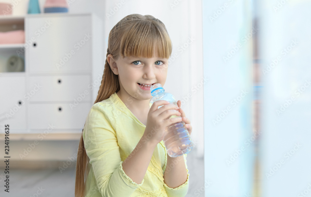 Cute little girl holding bottle with water indoors