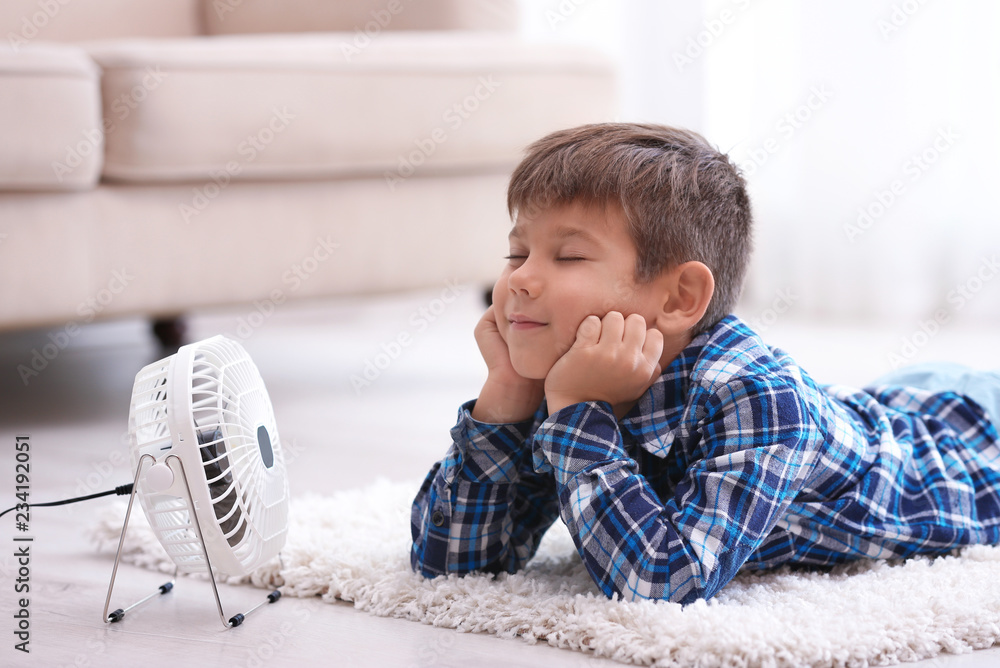 Obraz premium Little boy refreshing from heat in front of small fan at home