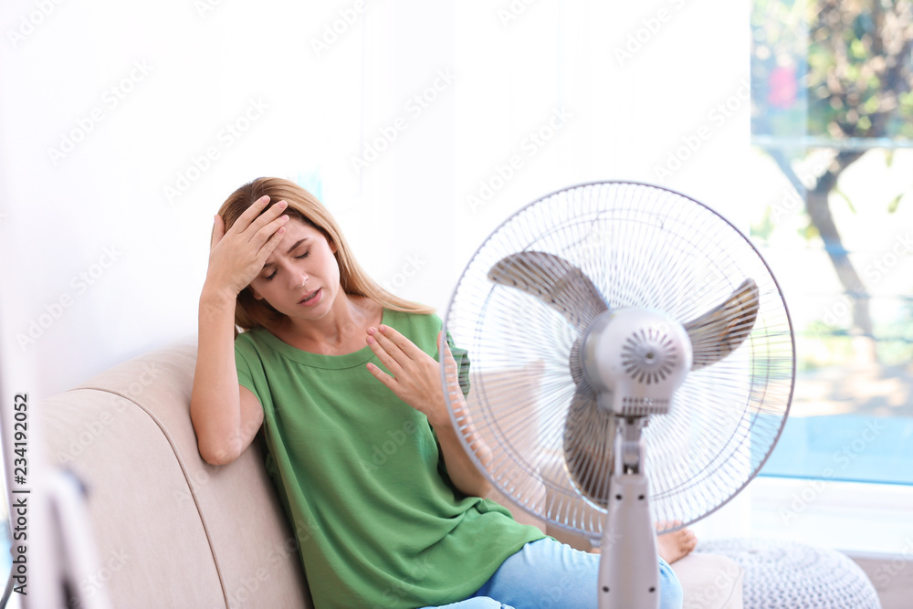 Fototapeta premium Woman suffering from heat in front of fan at home