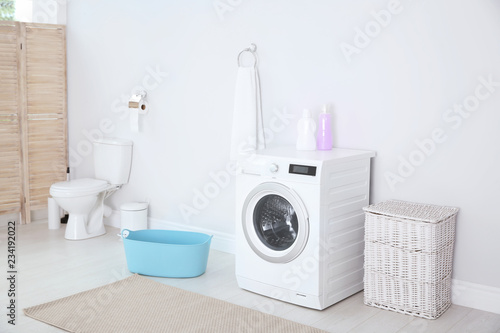 Modern washing machine in light bathroom interior