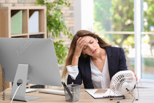 Fotografía Businesswoman suffering from heat in front of small fan at workplace