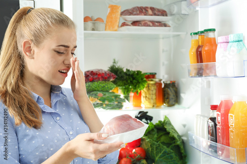 Woman taking stale meat out of refrigerator in kitchen