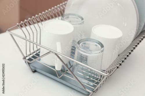 Dish drainer with clean dinnerware on table in kitchen