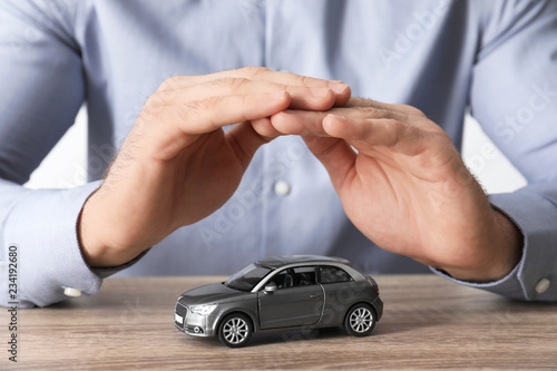 Male insurance agent covering toy car at table  closeup