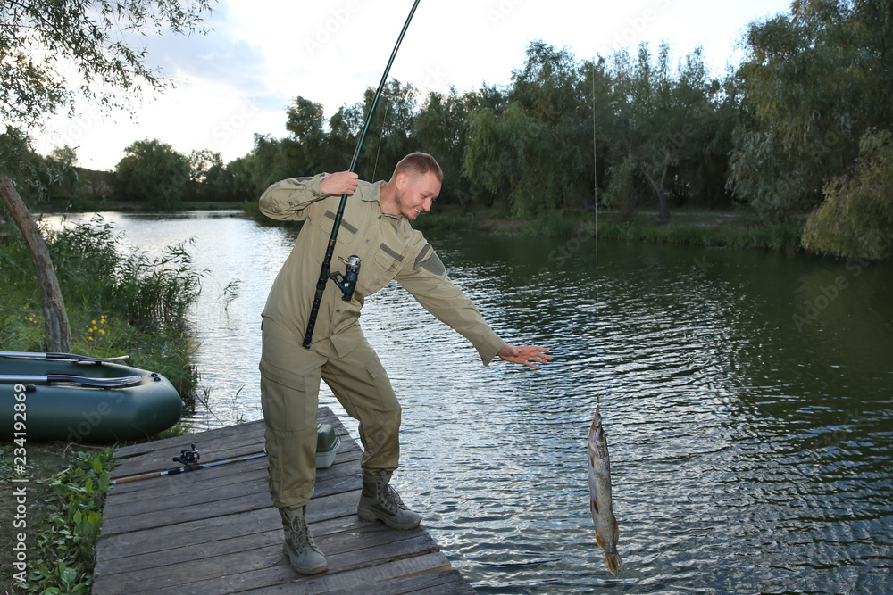 Man with rod and catch fishing on wooden pier at riverside. Recreational activity Man with rod and catch fishing on wooden pier at riverside. Recreational activity