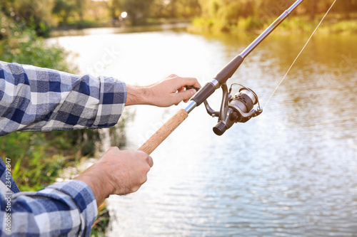 Man with rod fishing at riverside, focus on hands. Recreational activity