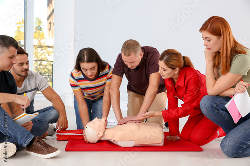 Group of people with instructor practicing CPR on mannequin at first aid class indoors