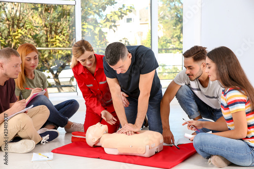 Group of people with instructor practicing CPR on mannequin at first aid class indoors photo