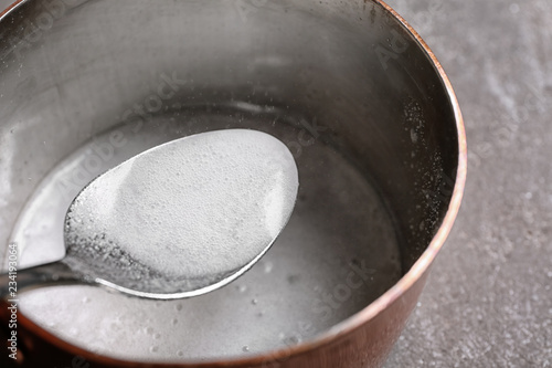 Chemical reaction of vinegar and baking soda in spoon over saucepan on table