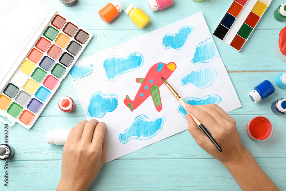Fototapeta premium Girl painting picture of airplane on table, top view