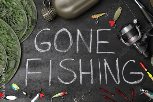 Flat lay composition with angling equipment and words "GONE FISHING" on dark background
