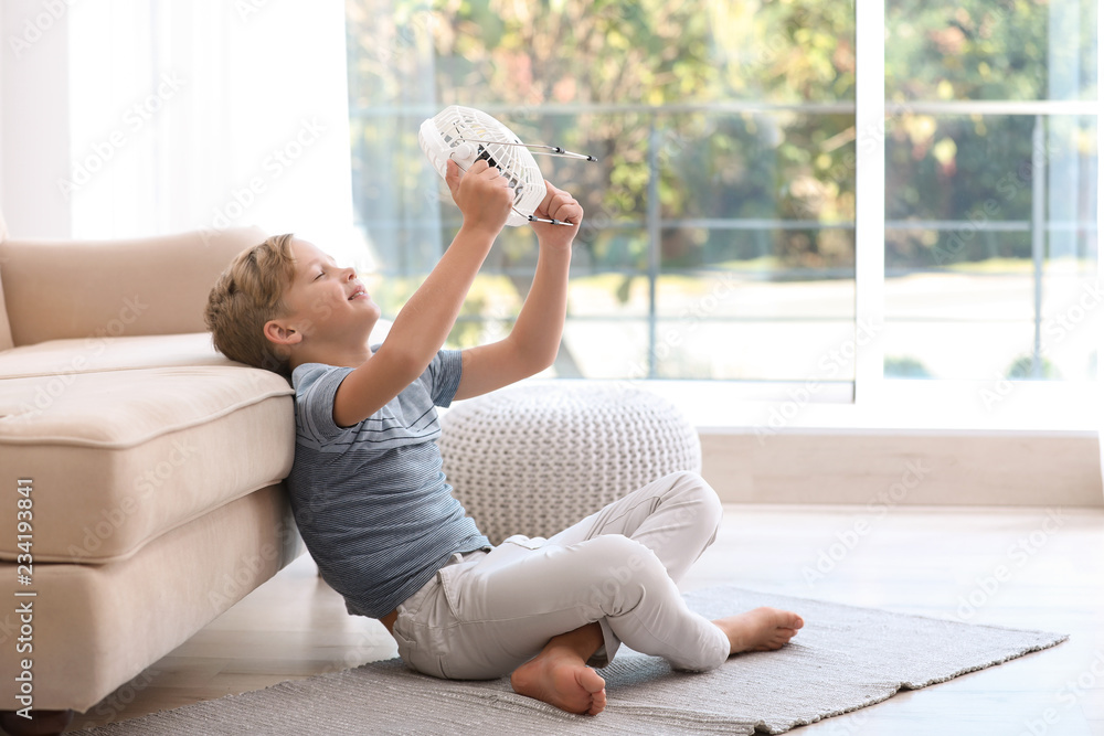 Naklejka premium Little boy with fan relaxing at home. Summer heat