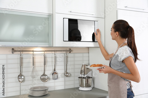 Young woman with plate of croissants near microwave oven in kitchen