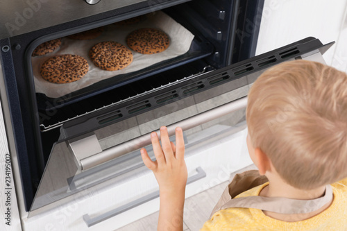 Little boy baking cookies in oven at home