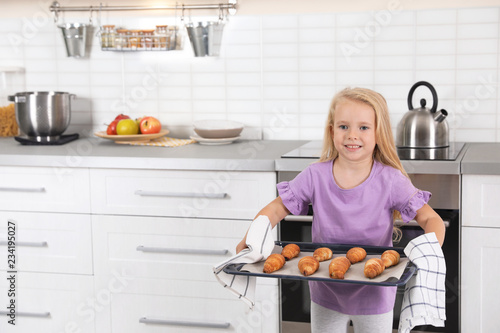 Little girl holding baking sheet with homemade oven baked croissants in kitchen